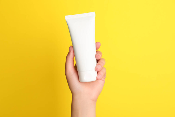 Woman holding tube of face cream on yellow background, closeup - 写真・画像