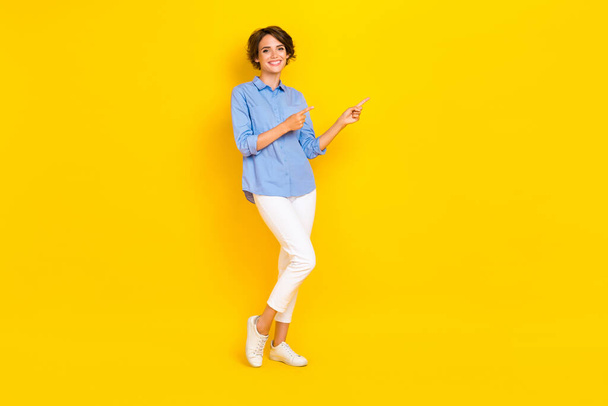 Full length photo of positive pretty lady wear blue shirt pointing two fingers empty space isolated yellow color background. - Foto, Imagem