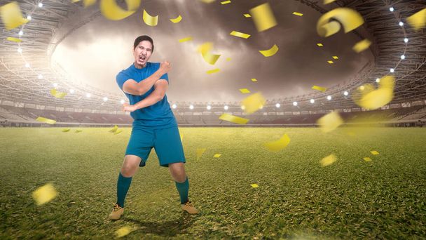 Asian football player man in a blue jersey celebrates the victory on the football field - 写真・画像