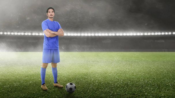 Asian football player man in a blue jersey standing with the ball on the football field - Fotografie, Obrázek