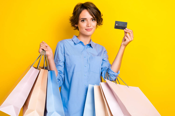 Photo of sweet shiny girl dressed blue shirt rising credit card bargains isolated yellow color background. - Foto, imagen