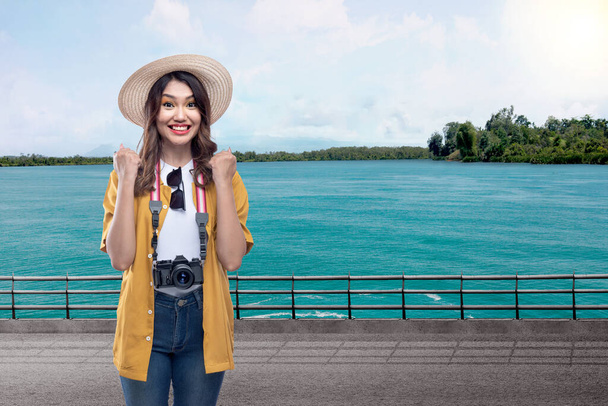 Asian woman with a hat and camera with an excited expression with lake and blue sky background - Foto, Bild