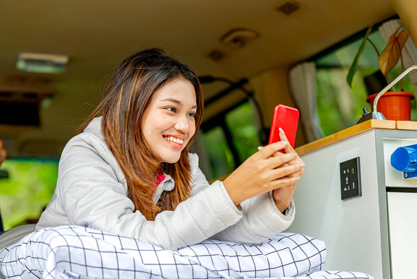 Asian woman using mobile phone inside the campervan enjoying camp activity in nature - Fotó, kép
