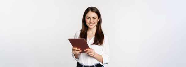 Retrato de mulher corporativa sorridente olhando para tablet digital, trabalhando, de pé sobre fundo branco. - Foto, Imagem