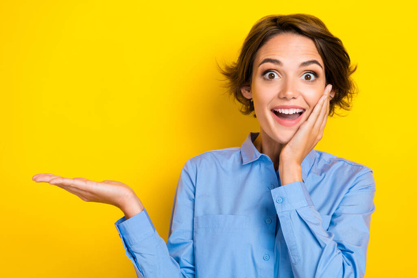 Closeup photo of young gorgeous woman wear blue office business shirt touch cheeks shock hold hand promoter deal isolated on yellow color background. - 写真・画像