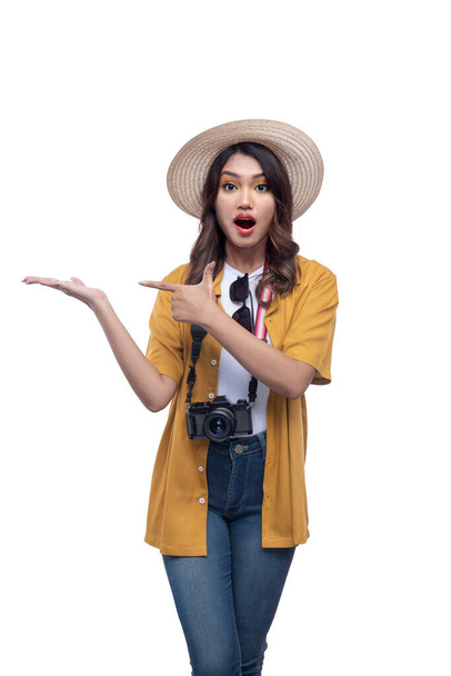 Asian woman with a hat and camera with open palm pointing at something isolated over white background - Foto, Imagem