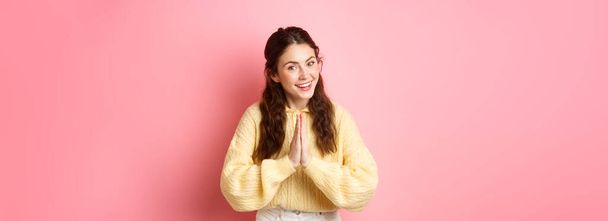 Thank you. Smiling polite girl greeting you with namaste gesture, bowing and looking friendly, express gratitude, being thankful, standing over pink background. - Фото, зображення