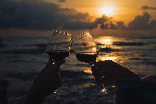 Zbliżenie sylwetka dwóch kieliszków wina brzęczących na tle pięknego zachodu słońca nad morzem. Pojęcie świętowania, romansu, przyjaźni - Zdjęcie, obraz