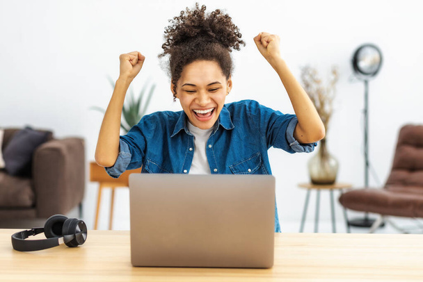 Happy female office worker working, having good news she receive payment. Portrait of excited young African American woman celebrating success sitting workplace in the office with laptop - Fotoğraf, Görsel