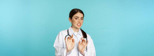 Image of woman doctor cringe, looking with dislike or aversion, rejecting, saying no, stay away, step back from something ugly, standing over torquoise background. - Foto, afbeelding