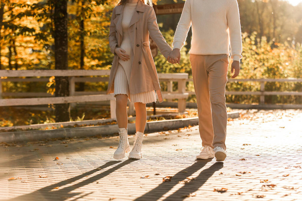 Запалена фотографія пари, чоловік і вагітна дружина тримаються за руки і ходять в осінній парку на заході сонця. Щаслива родина, яка любить вагітність. Поняття Дня матері і жіночого дня - Фото, зображення