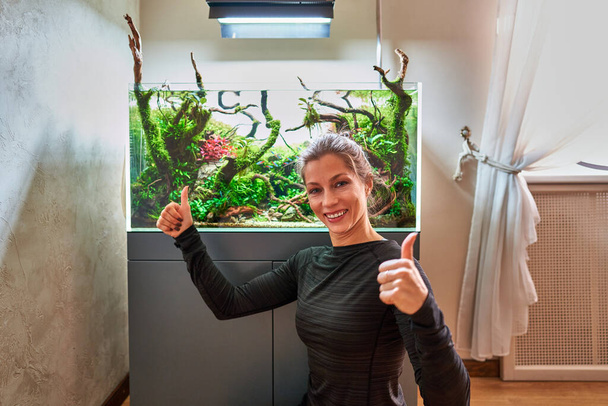 A beautiful smiling woman with thumbs up in front of aquarium aquascape. - Photo, Image