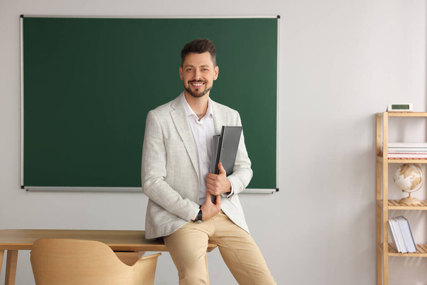 Happy teacher with stationery at desk in classroom - Foto, afbeelding