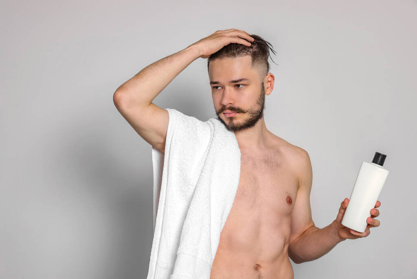 Naked man with towel and bottle of shampoo on light grey background - Φωτογραφία, εικόνα