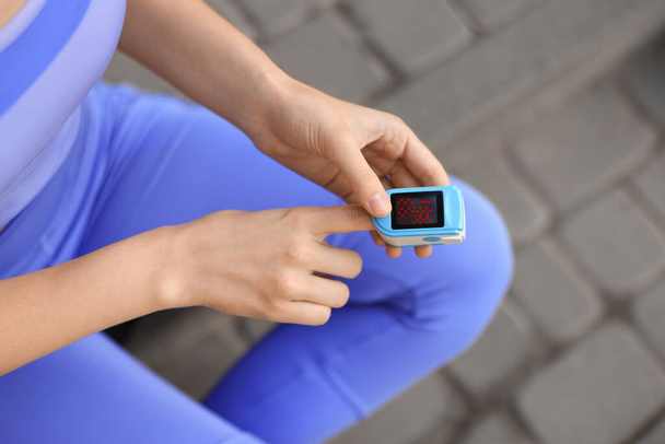 Woman checking pulse with blood pressure monitor on finger after training outdoors, closeup - Fotografie, Obrázek