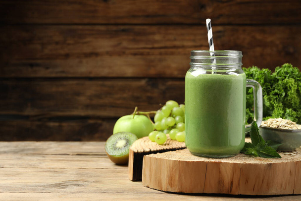 Mason jar of fresh green smoothie and ingredients on wooden table, space for text - Foto, Bild