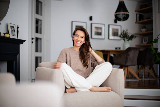Portrait of beautiful long haired woman wearing casual clothes while relaxing in an armchair at home.  - Foto, Bild