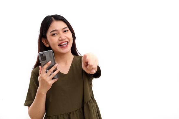 Szczęśliwa młoda Azjatka stojąca trzymając komórkę i patrząc w kamerę. Odizolowane na biało - Zdjęcie, obraz