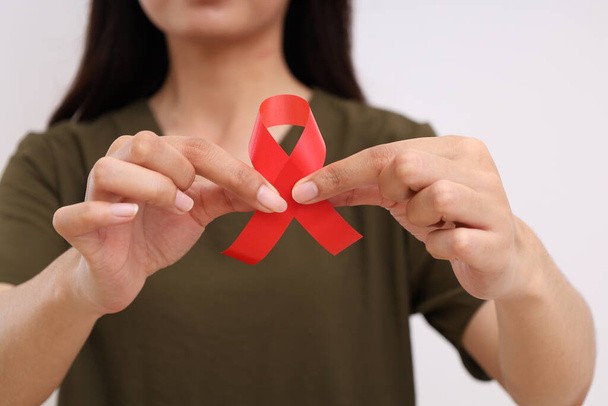 Detailní záběr ženské ruky držící červenou stuhu. Koncept kampaně na AIDS. Izolováno s kopírovacím prostorem - Fotografie, Obrázek