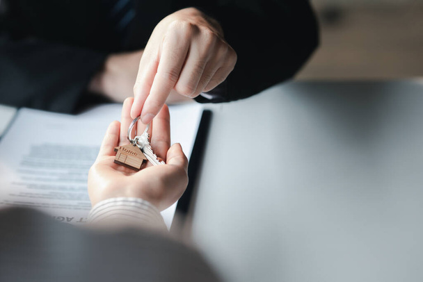 A home rental company employee is handing the house keys to a customer who has agreed to sign a rental contract, explaining the details and terms of the rental. Home and real estate rental ideas. - Foto, afbeelding