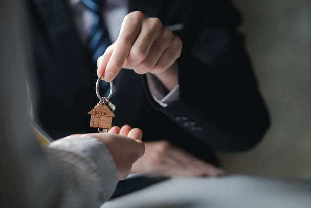 A home rental company employee is handing the house keys to a customer who has agreed to sign a rental contract, explaining the details and terms of the rental. Home and real estate rental ideas. - 写真・画像