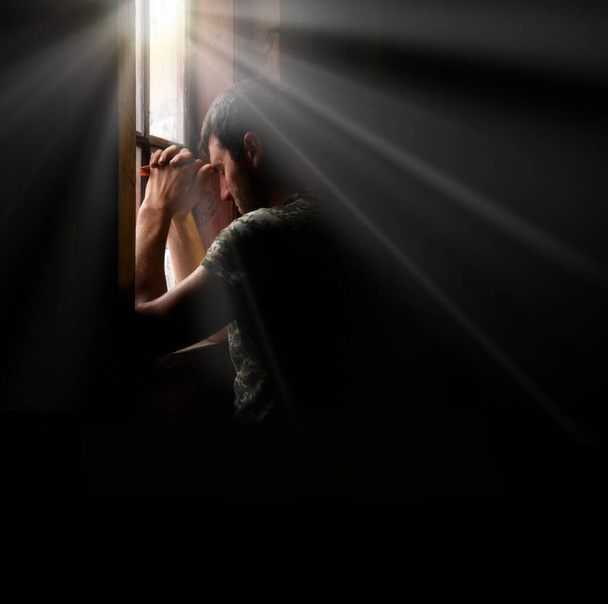 Tired pensive devote belief navy force young guy hero face cry hope hand pain love dark black old retro home room sun light text space. Worry human feel lost despair frown upset warfare believe concept - Photo, Image
