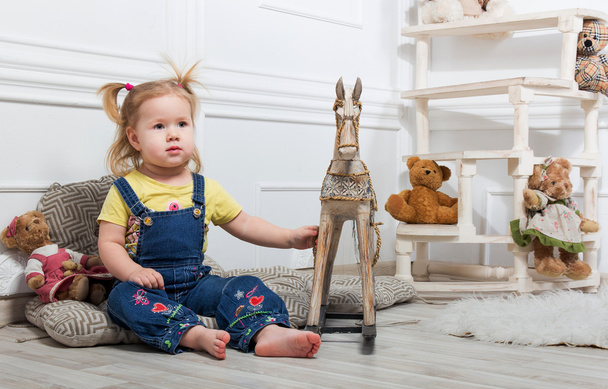 Little girl  surrounded by toys and holds a wooden horse - Φωτογραφία, εικόνα