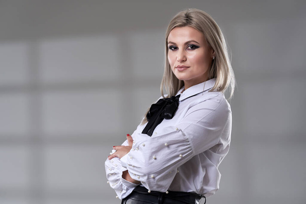 Closeup of a young blonde businesswoman with white shirt and black skirt on gray background - Foto, immagini