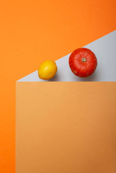 Геометрический натюрморт с созревшей тыквой и лимоном на цветном фоне - Фото, изображение