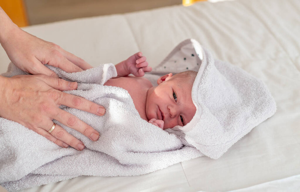 Мама сушит мягким полотенцем своего новорожденного ребенка после ежедневной ванны перед сном. Концепция ухода за новорожденными и гигиены - Фото, изображение