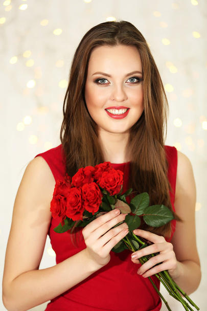 Smiling girl with bouquet of red roses on lights background - Foto, Imagen