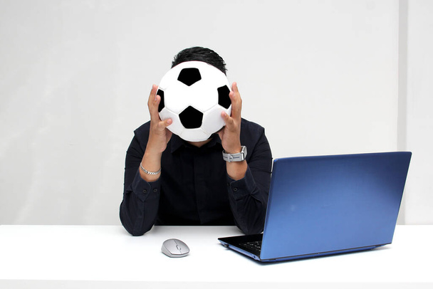 Взрослый латиноамериканец смотрит футбольные матчи на своем рабочем ноутбуке в рабочее время утром, он видит его взволнованным, нервным, удивленным рядом со своим футбольным мячом - Фото, изображение