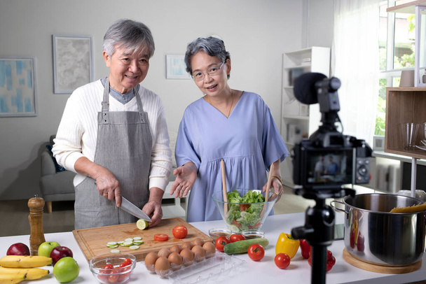 Glückliches asiatisches Seniorenpaar Blogger Vlogger und Online-Influencer Aufzeichnung von Videoinhalten über gesunde Ernährung in der Küche. - Foto, Bild