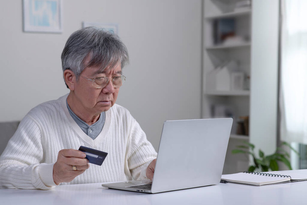 Спантеличений літній азіатський пенсіонер, який вийшов на пенсію, підкреслив, що засмучений чоловік має проблеми з оплатою, покупкою онлайн, платежами з кредитною заблокованою банківською карткою, ноутбуком. Інтернет шахрайство - Фото, зображення
