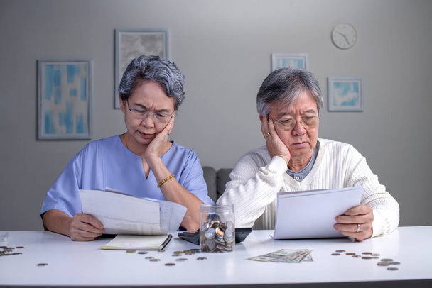 Preocupada pareja asiática de ancianos leyendo documentos financieros o una carta de notificación con malas noticias del banco mientras pagan facturas, el esposo y la esposa jubilados tienen problemas de dinero - Foto, Imagen