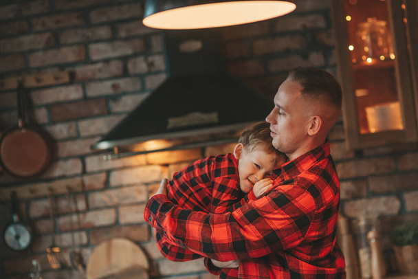 赤い小さな息子を持つ笑顔活動的な両親は、サンタの屋内を待っているチェッカー付きの眠りにつく。スタイリッシュな家族の愛笑い抱擁自宅でキス。新年のガーランドとライトを祝う12月25日ノエルの木 - 写真・画像