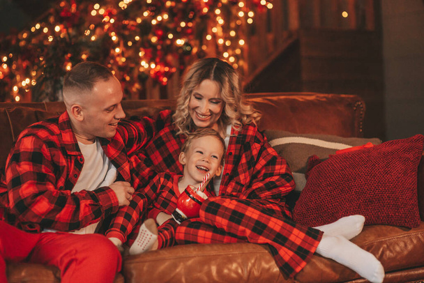 Kırmızı kareli elbiseli, Noel Baba 'yı evde bekleyen küçük oğlu olan aktif ailelere gülümseyin. Tarz sahibi aile, gülüşlere, kucaklaşmalara evde sarılmaya bayılır. 25 Aralık Noel Ağacı 'nın yeni yıl çelenkleri ve ışıkları kutlanır - Fotoğraf, Görsel