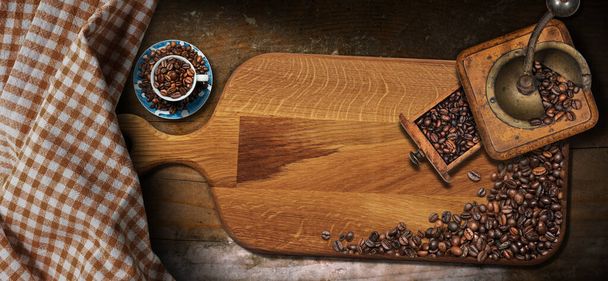 Ancien moulin à café manuel vintage avec grains de café torréfiés, tasse, planche à découper et nappe à carreaux blancs et marron sur une table en bois avec espace de copie. - Photo, image