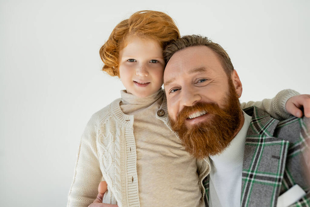 Portrait of positive man in jacket hugging son and looking at camera isolated on grey  - Foto, afbeelding