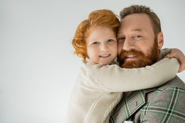 Pozitív vörös hajú fiú kötött pulcsiban átöleli apát elszigetelve a szürkén  - Fotó, kép