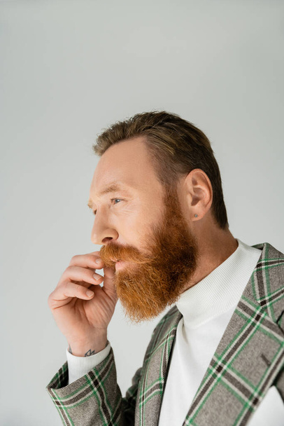 Portrait of bearded man in plaid jacket touching moustache isolated on grey  - Foto, afbeelding