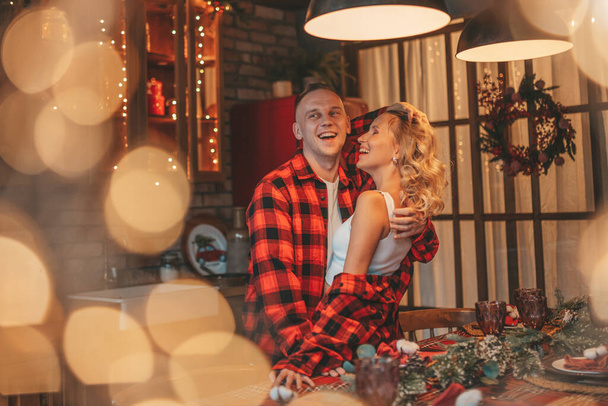 Портрет молодої милої пари, що обіймає кімнату напередодні 25 грудня. Любителям сміються обійми поцілунки, які чекають дива вдома. Святкування Нового року гірлянди запалюють ноель в червоній піжамі ніжності
 - Фото, зображення