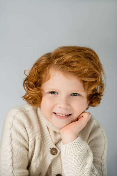 Gri renkli kameraya bakarak örgü ören kızıl saçlı çocuğun portresi.  - Fotoğraf, Görsel