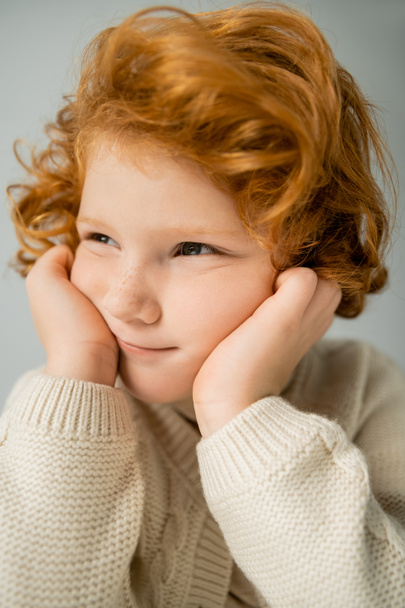 Portrait of red haired kid in beige knitted jumper looking away isolated on grey  - Photo, Image