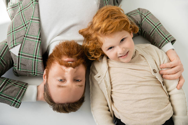top view of redhead dad and son in stylish clothing lying on grey background - Fotografie, Obrázek