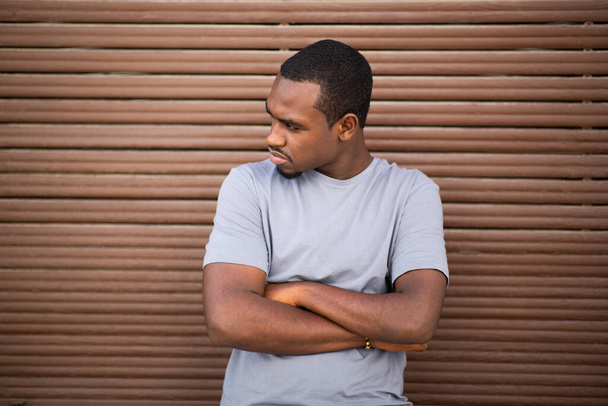Portrait of black man with arms crossed looking away standing against wood background - Фото, зображення
