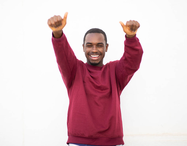 Πορτρέτο του χαρούμενος νεαρός μαύρος δείχνει τους αντίχειρες επάνω με τα δύο χέρια ενάντια στο λευκό τοίχο - Φωτογραφία, εικόνα