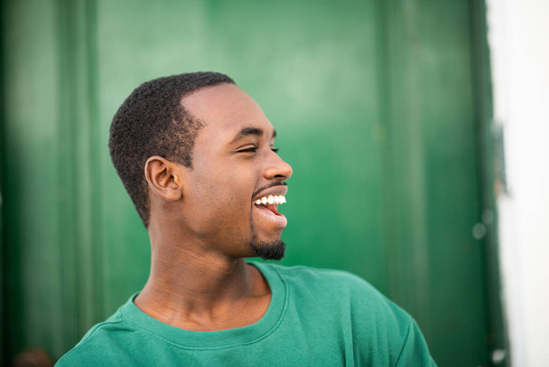 Close up side portrait of cheerful young african man smiling against green background - Photo, Image