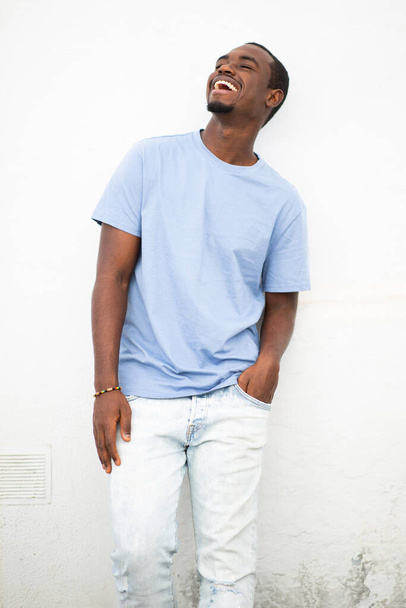 Portret van een stijlvolle jonge zwarte man glimlachend tegen een witte muur - Foto, afbeelding