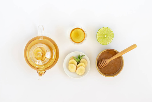 Draufsicht auf eine Tasse Tee mit Ingwerwurzel, Limette, Zimt und Teekanne auf weißem Hintergrund. Gesundheitsgetränk. - Foto, Bild